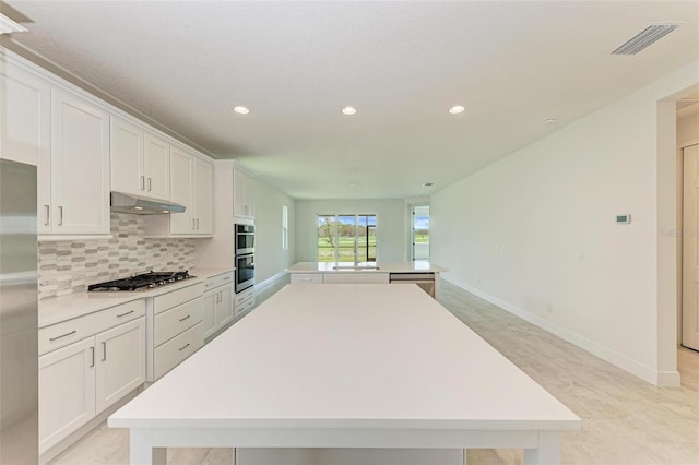 kitchen featuring white cabinets, appliances with stainless steel finishes, a spacious island, and tasteful backsplash