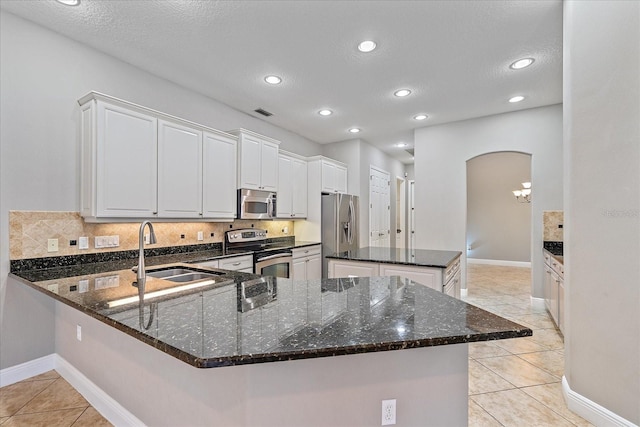 kitchen featuring dark stone countertops, light tile patterned floors, appliances with stainless steel finishes, white cabinetry, and sink