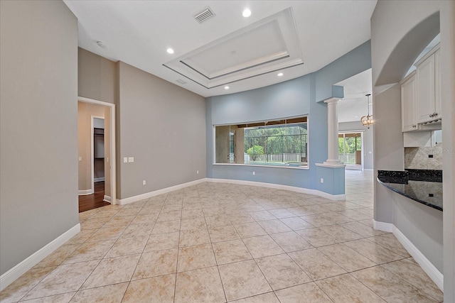 kitchen with dark stone countertops, white cabinetry, light tile patterned floors, decorative columns, and a tray ceiling