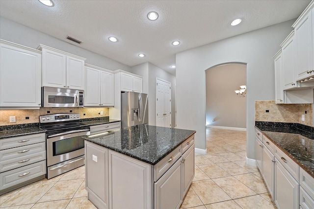 kitchen with a textured ceiling, a kitchen island, backsplash, appliances with stainless steel finishes, and white cabinets