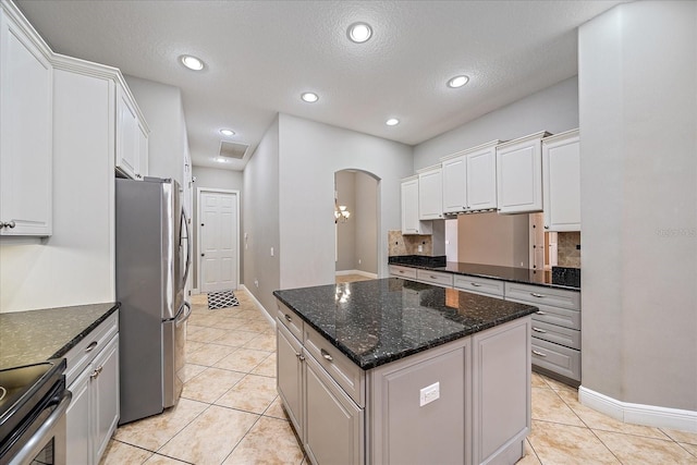 kitchen featuring a kitchen island, light tile patterned floors, appliances with stainless steel finishes, white cabinetry, and dark stone counters