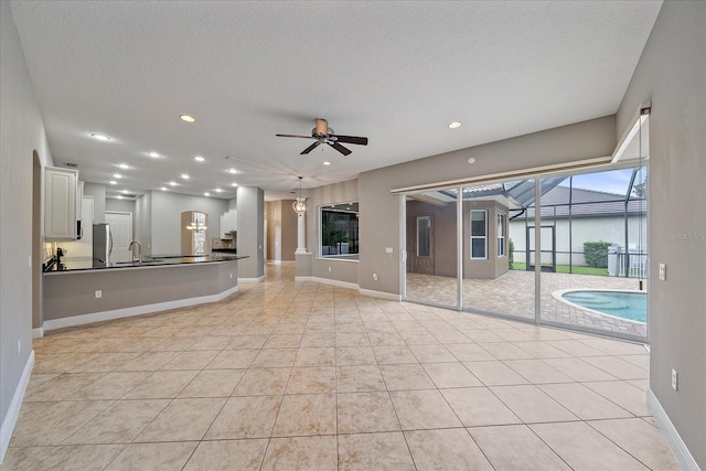 unfurnished living room with a textured ceiling, ceiling fan, sink, and light tile patterned floors