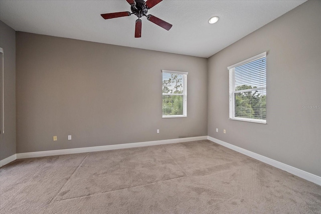 spare room featuring ceiling fan, a wealth of natural light, and light carpet