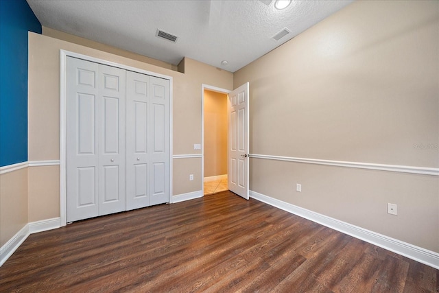 unfurnished bedroom with a textured ceiling, dark wood-type flooring, and a closet