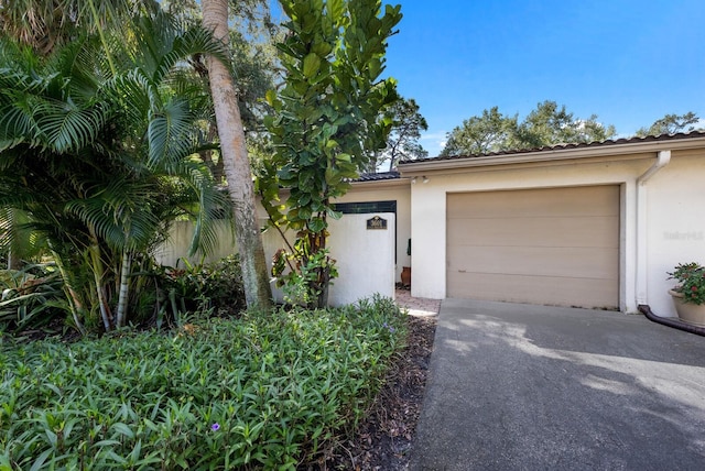 view of front of house featuring driveway, a tiled roof, an attached garage, and stucco siding