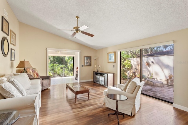 living room featuring wood-type flooring, vaulted ceiling, a textured ceiling, and ceiling fan