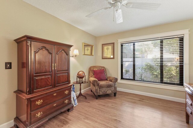 living area with a textured ceiling, light hardwood / wood-style flooring, and ceiling fan