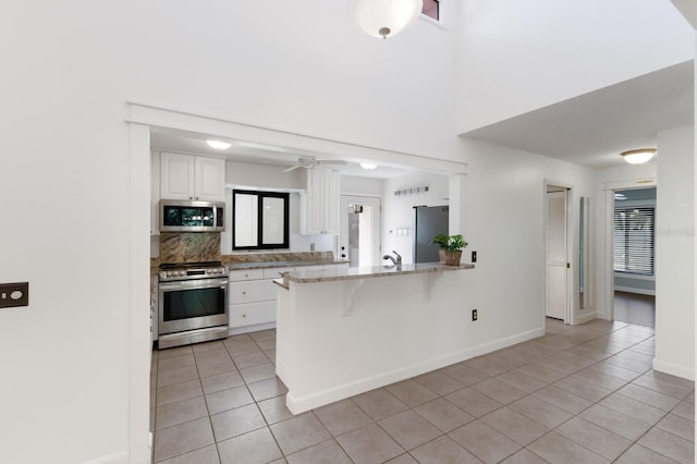 3601 Quail Hollow Ln, Bradenton, FL 34210 - kitchen with appliances with stainless steel finishes, light tile patterned floors, white cabinets, a kitchen breakfast bar, and a towering ceiling