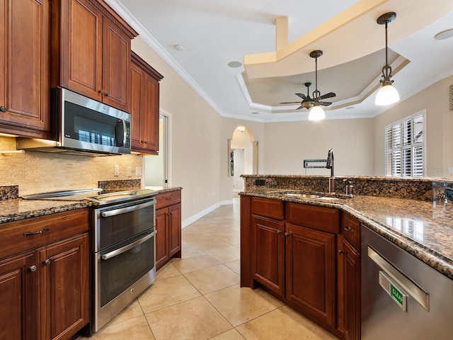 kitchen with appliances with stainless steel finishes, a tray ceiling, crown molding, sink, and light tile patterned floors