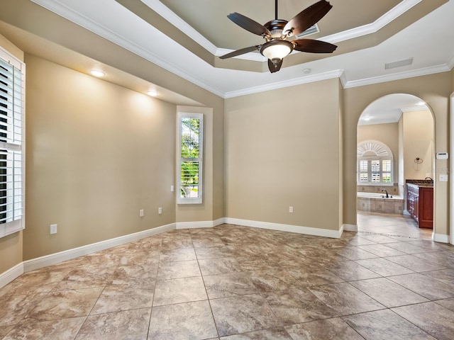 empty room featuring a raised ceiling, ceiling fan, ornamental molding, and sink