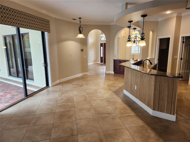 kitchen featuring pendant lighting, dark stone counters, crown molding, and light tile patterned floors