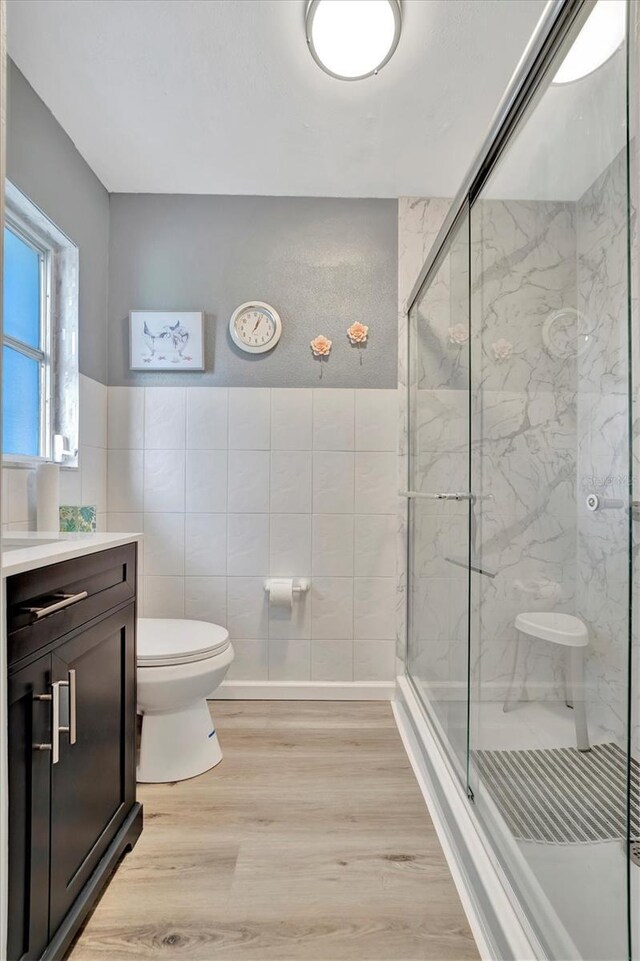 bathroom featuring toilet, vanity, wood-type flooring, tile walls, and a shower with shower door