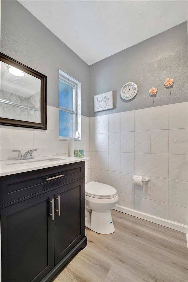 bathroom featuring hardwood / wood-style flooring, toilet, tile walls, vanity, and a textured ceiling