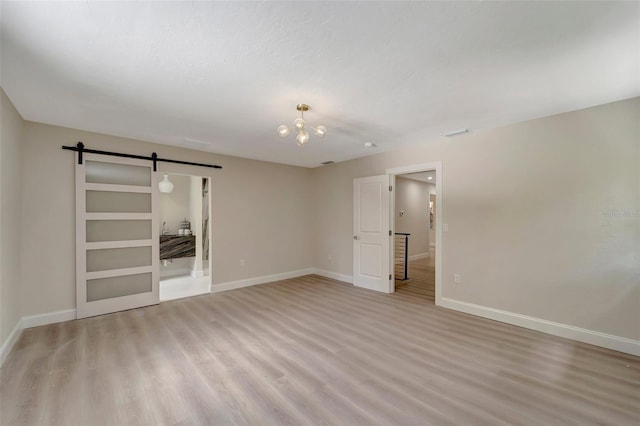 unfurnished room with a barn door, light hardwood / wood-style floors, and a notable chandelier