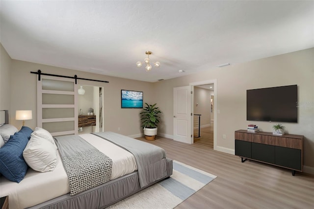 bedroom featuring light wood-type flooring, a chandelier, and a barn door