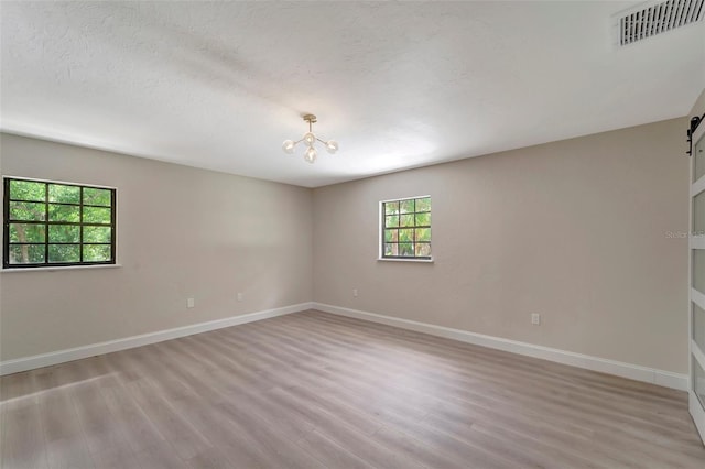 unfurnished room with an inviting chandelier, light wood-type flooring, a textured ceiling, and a barn door