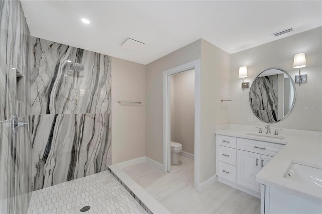 bathroom with tiled shower, vanity, and toilet