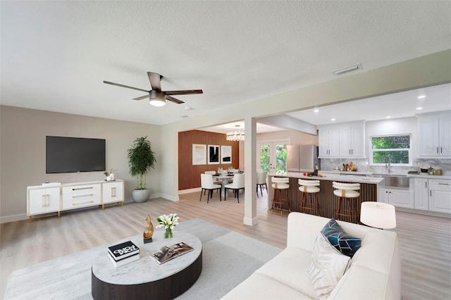 living room with a textured ceiling, a healthy amount of sunlight, ceiling fan with notable chandelier, and light hardwood / wood-style flooring