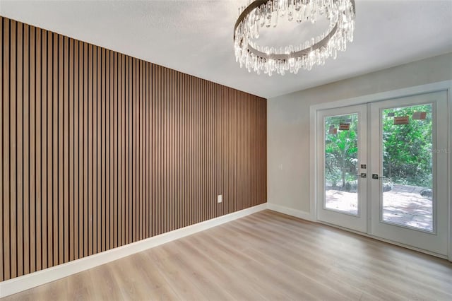 empty room with french doors, a textured ceiling, wooden walls, light hardwood / wood-style flooring, and an inviting chandelier