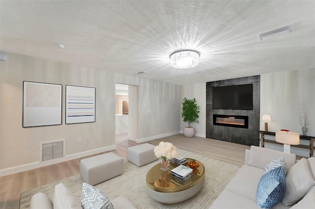 living room featuring a textured ceiling, light hardwood / wood-style floors, and a large fireplace