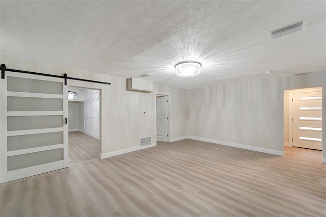 basement with light wood-type flooring, a textured ceiling, a barn door, and built in shelves