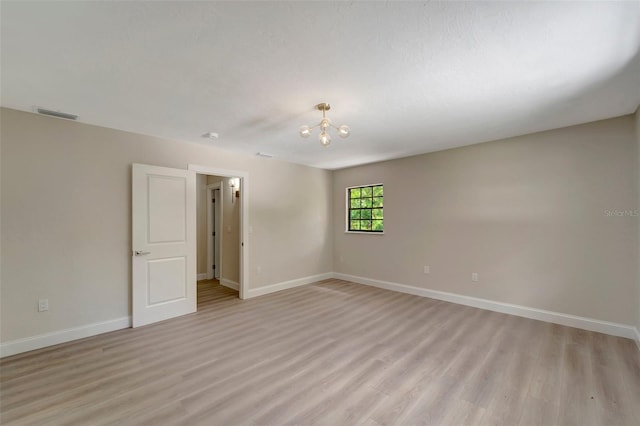 empty room with light hardwood / wood-style flooring and a chandelier