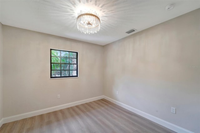 empty room featuring a notable chandelier and light wood-type flooring