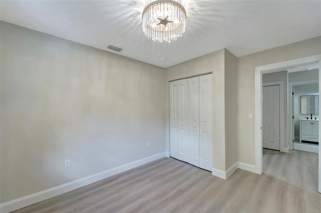 unfurnished bedroom featuring an inviting chandelier, a closet, and light hardwood / wood-style floors