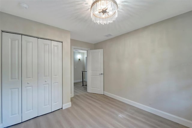 unfurnished bedroom featuring a notable chandelier, light hardwood / wood-style flooring, and a closet