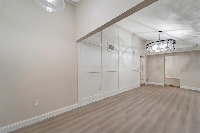 empty room with a notable chandelier, a textured ceiling, and light hardwood / wood-style floors