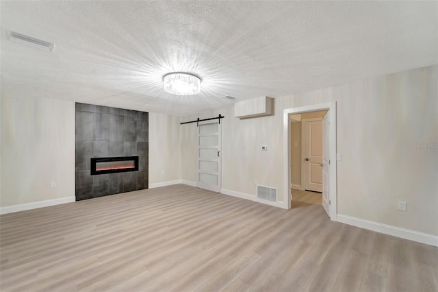 unfurnished living room with a textured ceiling, light wood-type flooring, a fireplace, and a barn door