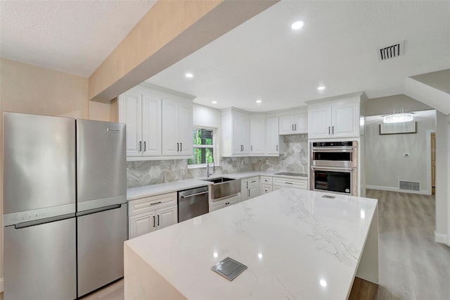 kitchen with light stone counters, stainless steel appliances, white cabinetry, and a center island