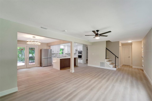 unfurnished living room with ceiling fan with notable chandelier, sink, light hardwood / wood-style flooring, and french doors