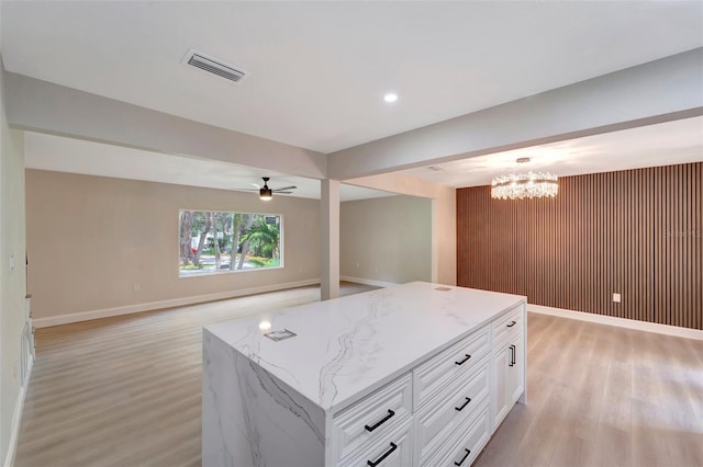 kitchen with light hardwood / wood-style floors, a kitchen island, light stone countertops, and white cabinetry