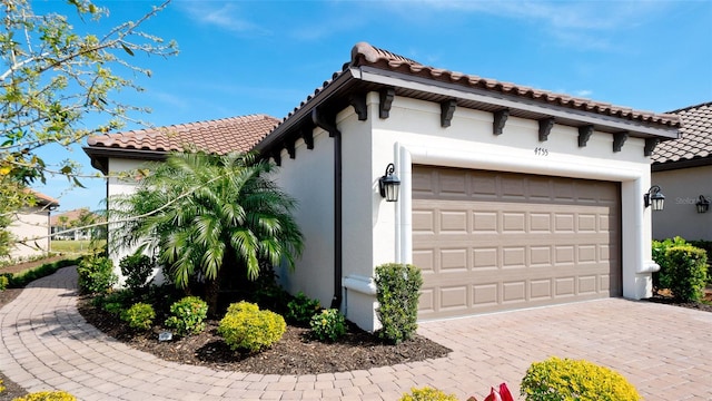 view of front of home with an attached garage, stucco siding, decorative driveway, and a tiled roof