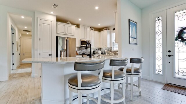 kitchen with a kitchen breakfast bar, light wood-type flooring, light stone countertops, tasteful backsplash, and stainless steel appliances