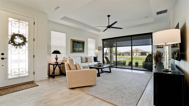 living room featuring ceiling fan, a healthy amount of sunlight, a raised ceiling, and light hardwood / wood-style floors