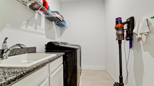 laundry room featuring washer and clothes dryer, cabinets, light wood-type flooring, and sink