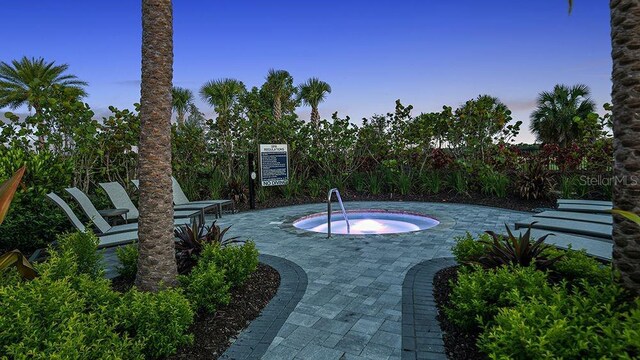 pool at dusk with a hot tub and a patio area