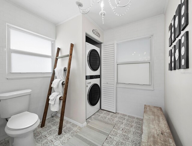 bathroom featuring crown molding, stacked washer and clothes dryer, toilet, and a notable chandelier