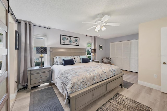 bedroom featuring a closet, a textured ceiling, light wood finished floors, baseboards, and a ceiling fan