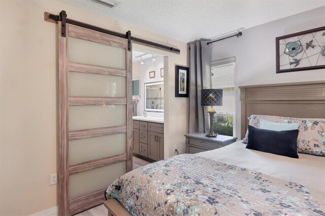 bedroom featuring a textured ceiling, ensuite bathroom, and a barn door