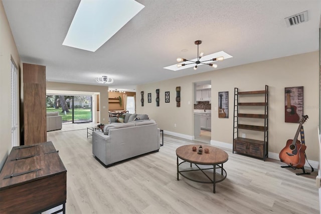 living area featuring a skylight, light wood finished floors, baseboards, a textured ceiling, and a chandelier