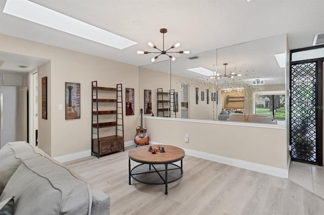 living area with a chandelier, a skylight, light wood-style flooring, and baseboards