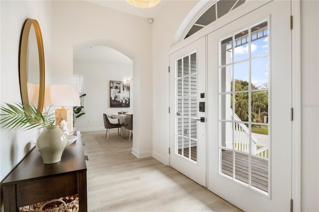 entryway featuring a healthy amount of sunlight, a notable chandelier, light hardwood / wood-style flooring, and french doors