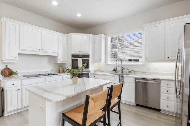 kitchen featuring white cabinets, appliances with stainless steel finishes, a center island, and light hardwood / wood-style flooring