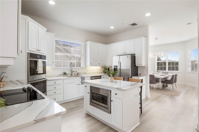 kitchen featuring light wood-type flooring, a chandelier, a center island, appliances with stainless steel finishes, and white cabinets