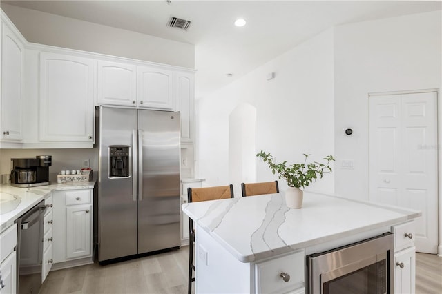 kitchen with a kitchen island, stainless steel appliances, light stone counters, and white cabinets