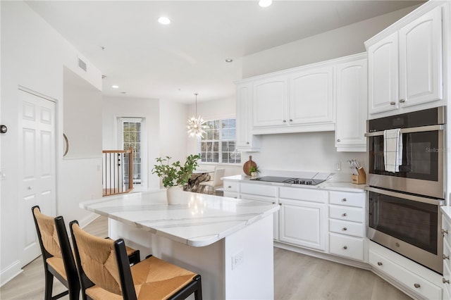 kitchen with light hardwood / wood-style floors, white cabinetry, black electric stovetop, light stone counters, and double oven