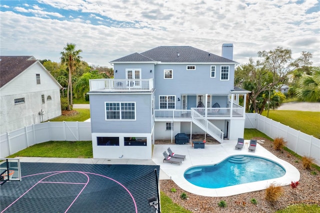 rear view of property with a balcony, a patio area, basketball hoop, a fenced in pool, and a yard